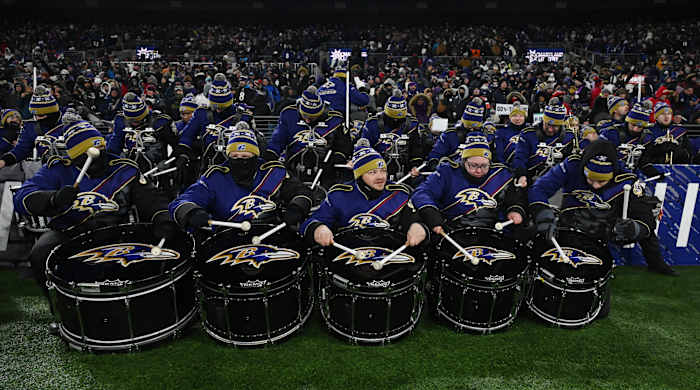Members of the Marching Ravens marching band sit on the sidelines ahead of a halftime performance